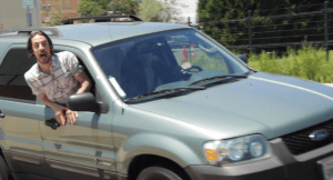 [Image: man leaning out of the passenger window of a car, yelling.]